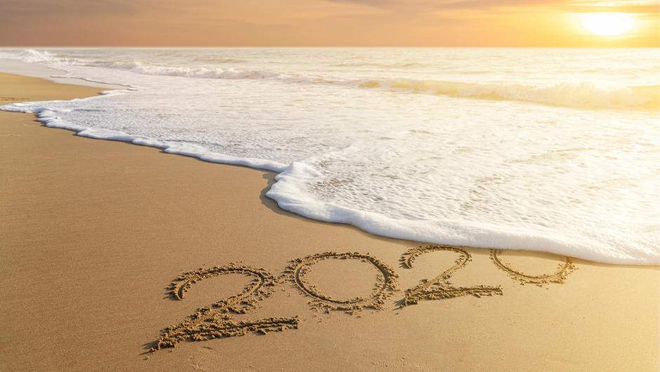 A wave washing away the number "2020" which has been written in the sand